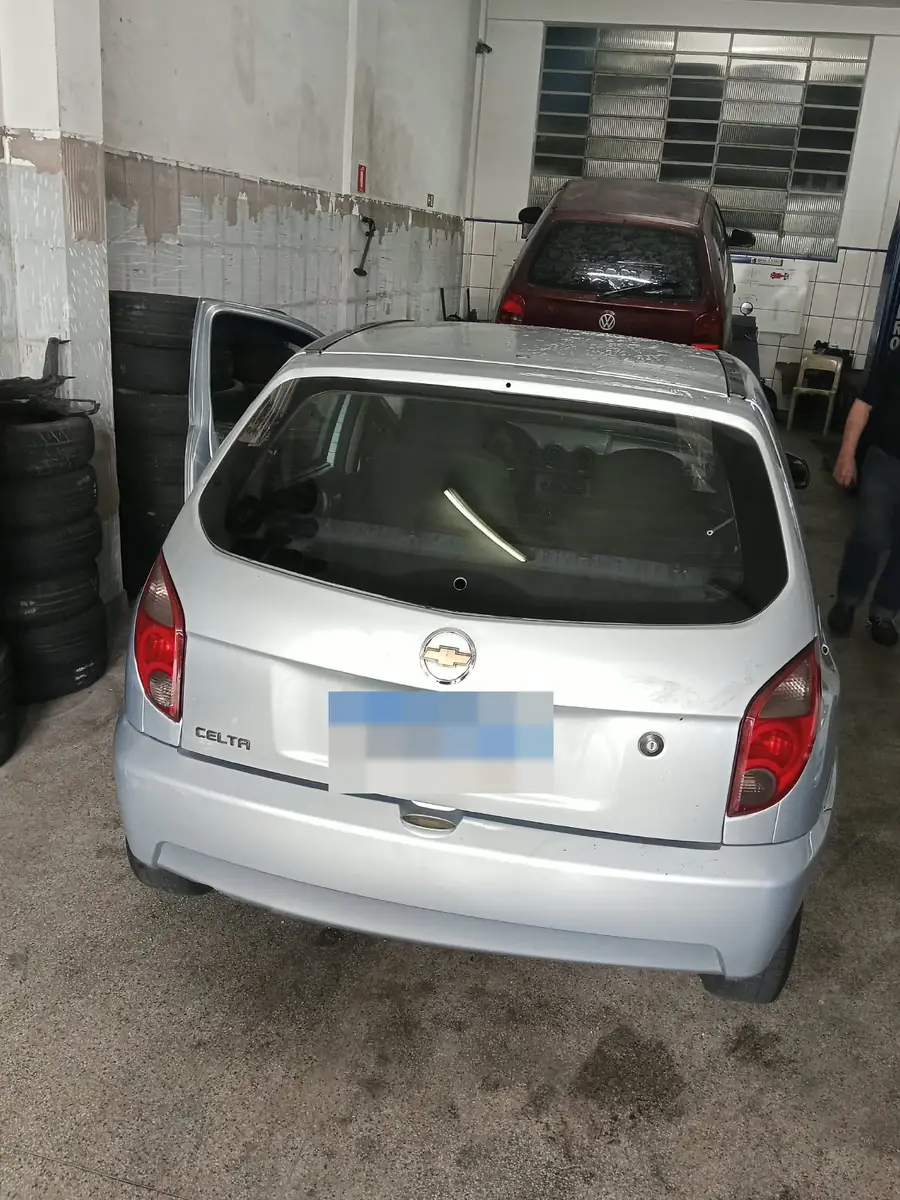 Traseira de um Chevrolet Celta prata na oficina após a troca do vidro traseiro, placa oculta.