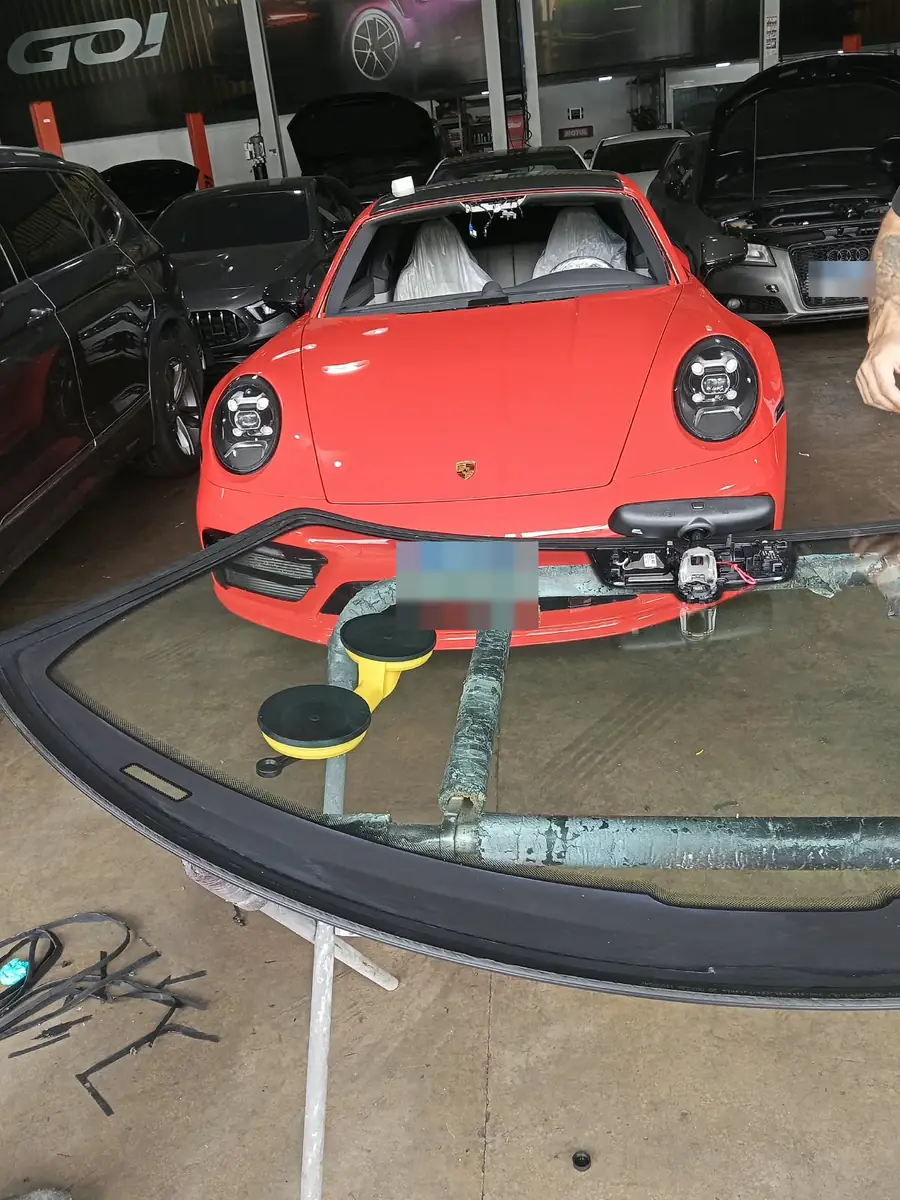 Para-brisa novo apoiado em suportes com ventosas, pronto para ser instalado no Porsche 911 vermelho.
