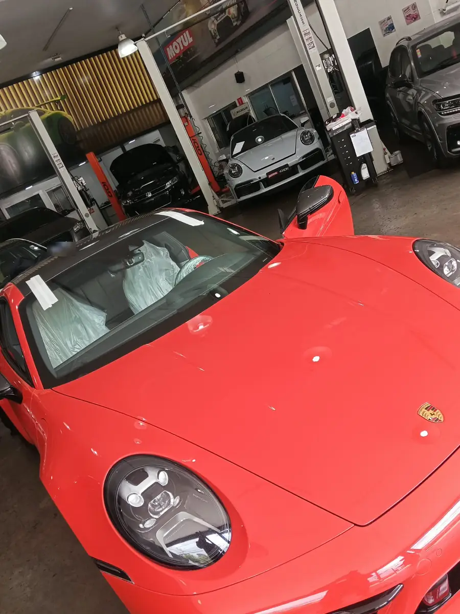 Porsche 911 vermelho na oficina, sem o para-brisa, com bancos protegidos para a troca.